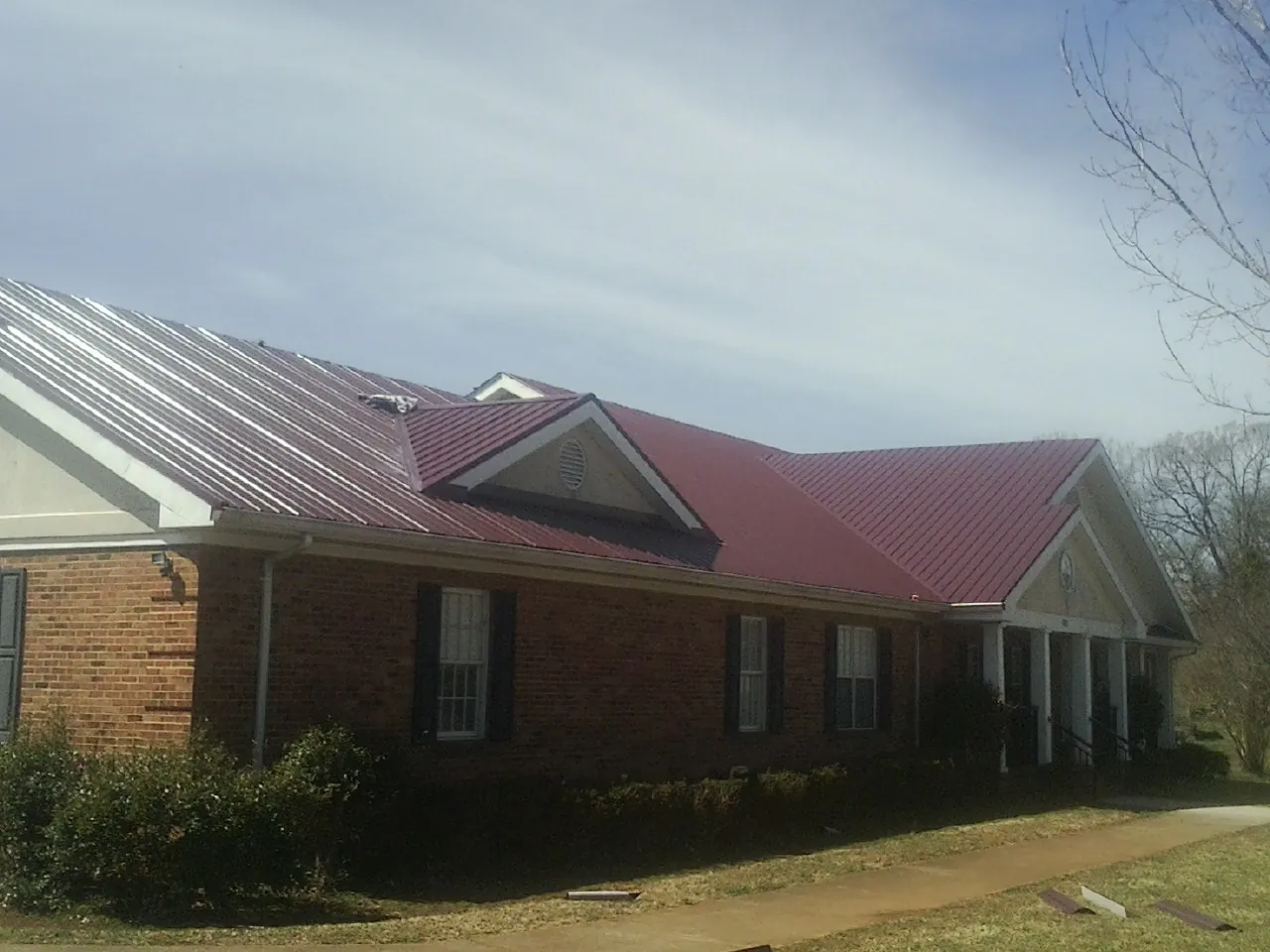 Red metal roof with gabled entries on a long brick building, from a Hail Damage Roof Repair job in Harrison